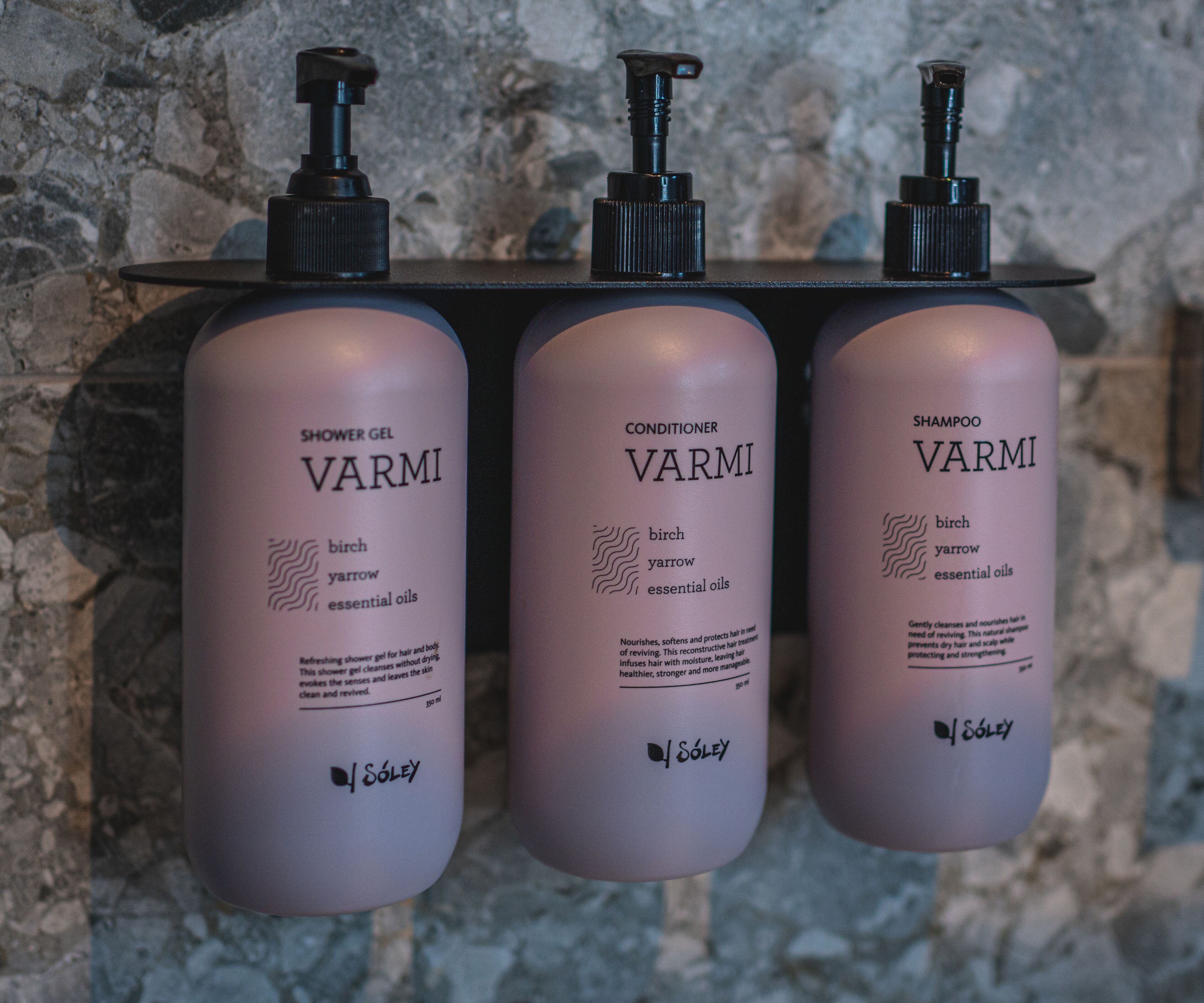 Three bottles of Varmi products on a shelf against a stone wall.
