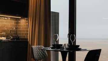 A modern dining area with a view of the sea, featuring a table set with wine glasses and a candle.