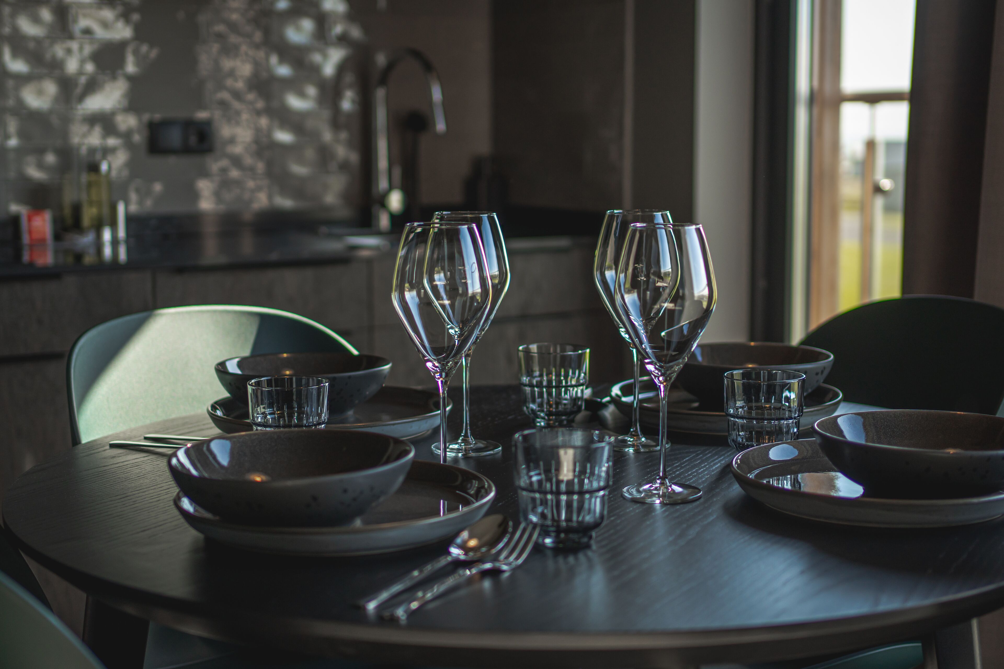 A dining table set with clear glassware and bowls, with a modern kitchen in the background.