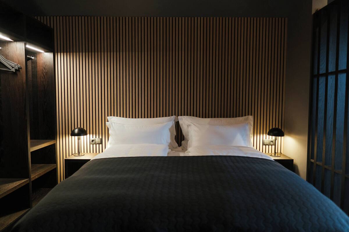 Habitación de hotel con cama, dos lámparas de noche, un panel de pared de listones de madera y un armario.