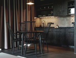 A modern kitchen with a dining area, featuring a dark wood cabinet, a stainless steel microwave, and a pendant light. - Black Beach Suites (Vik I Myrdal)