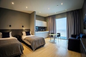 A hotel room with two beds, a kitchenette, a dining area, and a large window with curtains. - Black Beach Suites (Vik I Myrdal)