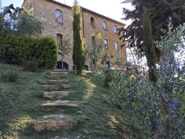 A stone building with a staircase leading up to a door, surrounded by greenery and trees. - Rocca degli Olivi (San Gimignano)