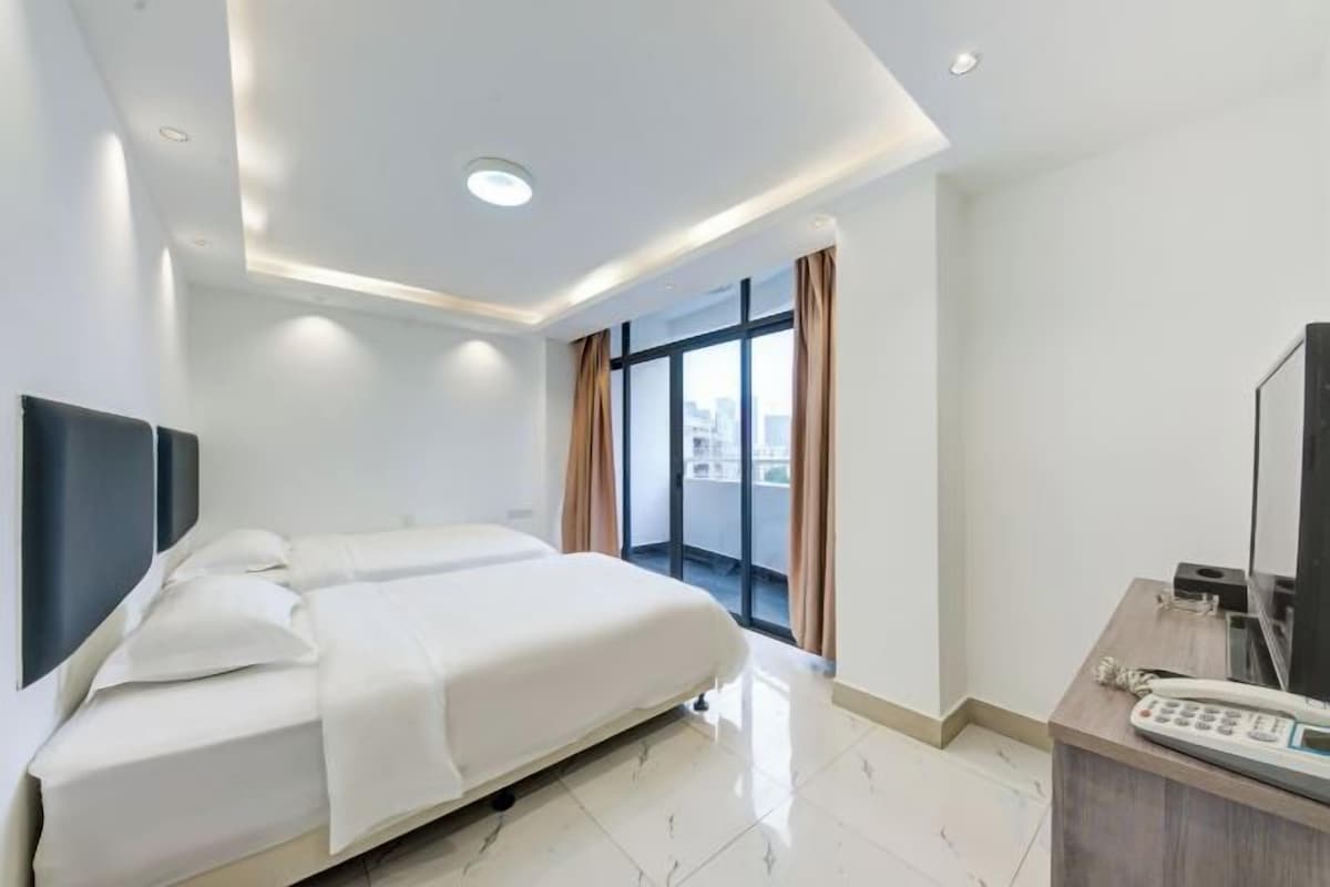 Una camera d'albergo moderna con un letto grande, una scrivania con il telefono e vista sulla città da ampie finestre.