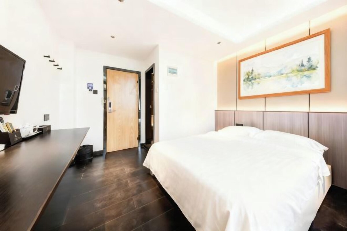 A hotel room with a bed, a desk with a flat-screen TV, and a painting on the wall.