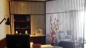 Una habitación con escritorio, silla, lámpara, estantería, planta en maceta y ventana con persianas.