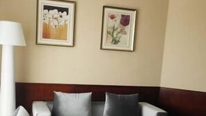 Una sala de estar con un sofá gris, una mesa de centro con un frutero, y dos cuadros florales enmarcados en la pared.
