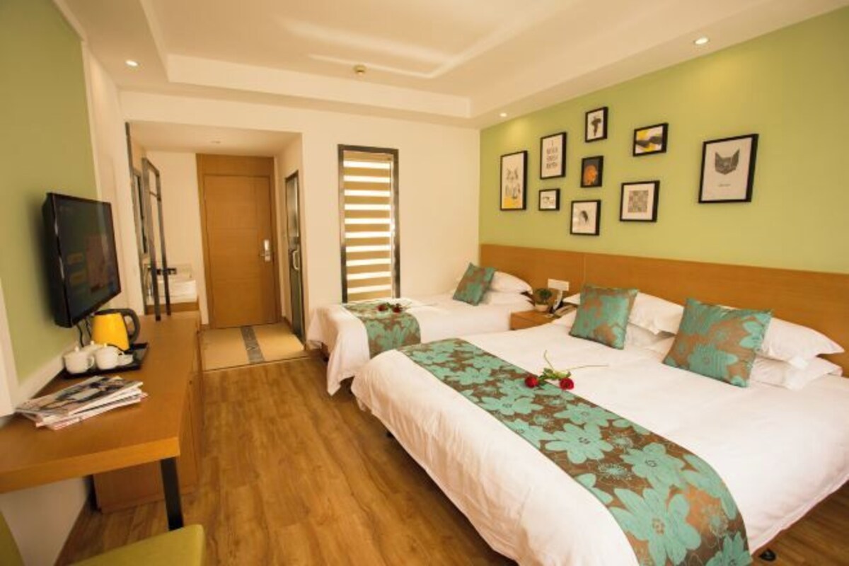 A hotel room with two beds, a desk with a chair, a television, and framed pictures on the wall.
