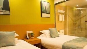 Habitación de hotel con dos camas, una mesita de noche con lámpara y cabina de ducha de vidrio.