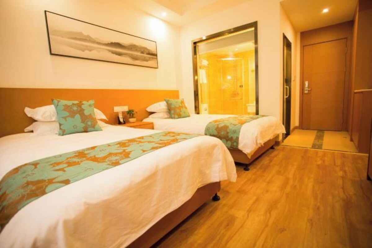 A hotel room with two beds, wooden flooring, a large mirror, and a painting on the wall.