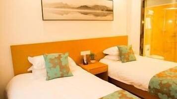 Habitación de hotel con dos camas, cada una con cubrecama y almohadas estampadas con motivos florales, una mesita de noche con lámpara y un cuadro enmarcado en la pared.