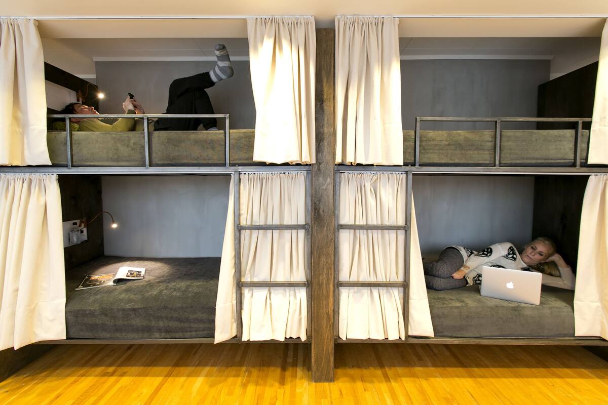 Habitación con literas de varios niveles, cortinas, una escalera y un ordenador portátil en la litera inferior.