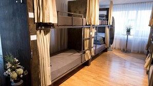 A bunk bed room with curtains, a small table with a plant, and a wooden floor. - B14 Hostel (Reykjavik)