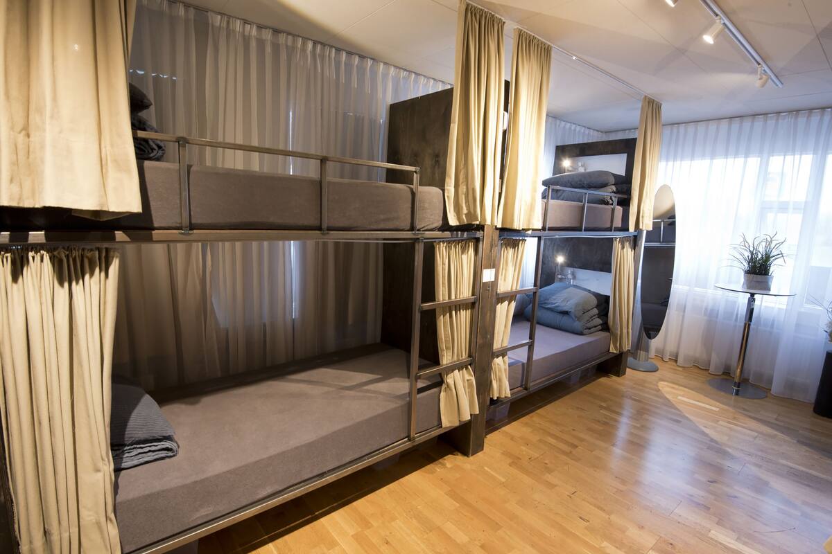 Dormitorio con literas, cortinas, una mesita con una planta y una ventana con cortinas traslúcidas.