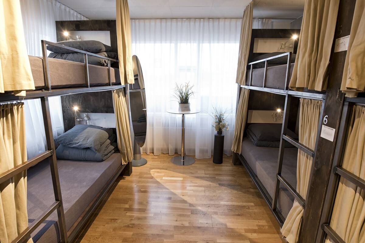 Habitación pequeña con literas, una mesita redonda con planta en maceta y vistas a través de cortinas translúcidas.