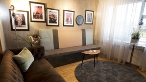 A cozy living room with a brown sofa, a round coffee table, a cushioned bench, and a large window with sheer curtains. - B14 Hostel (Reykjavik)