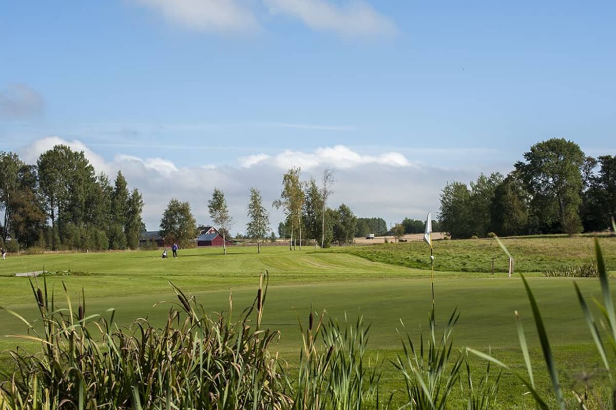 A golf course with a clubhouse, trees, and a clear sky.
