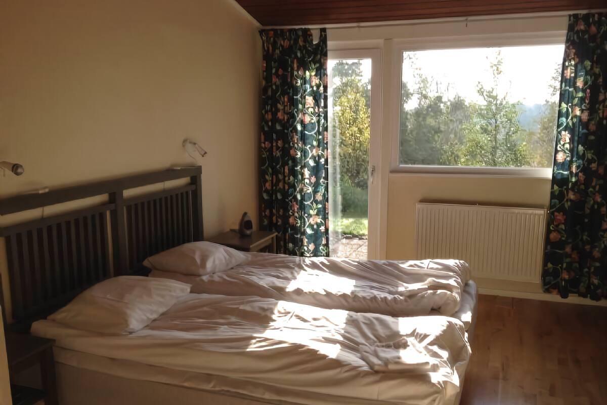 A bedroom with a wooden bed, a nightstand, and a window with curtains.