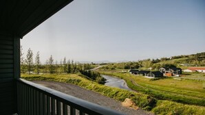 A view from a balcony overlooking a rural landscape with a river, houses, and greenery. - Guesthouse Hill (Hrunamannahreppur)