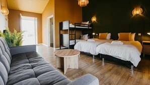 A modern hotel room with a sofa, two beds, a small table, and a large window. - Guesthouse Hill (Hrunamannahreppur)