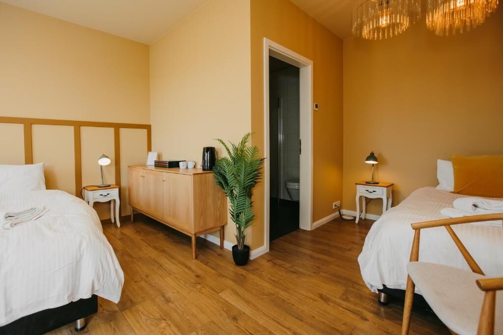 Habitación de hotel con dos camas, un aparador de madera, una planta en maceta y la puerta del baño.