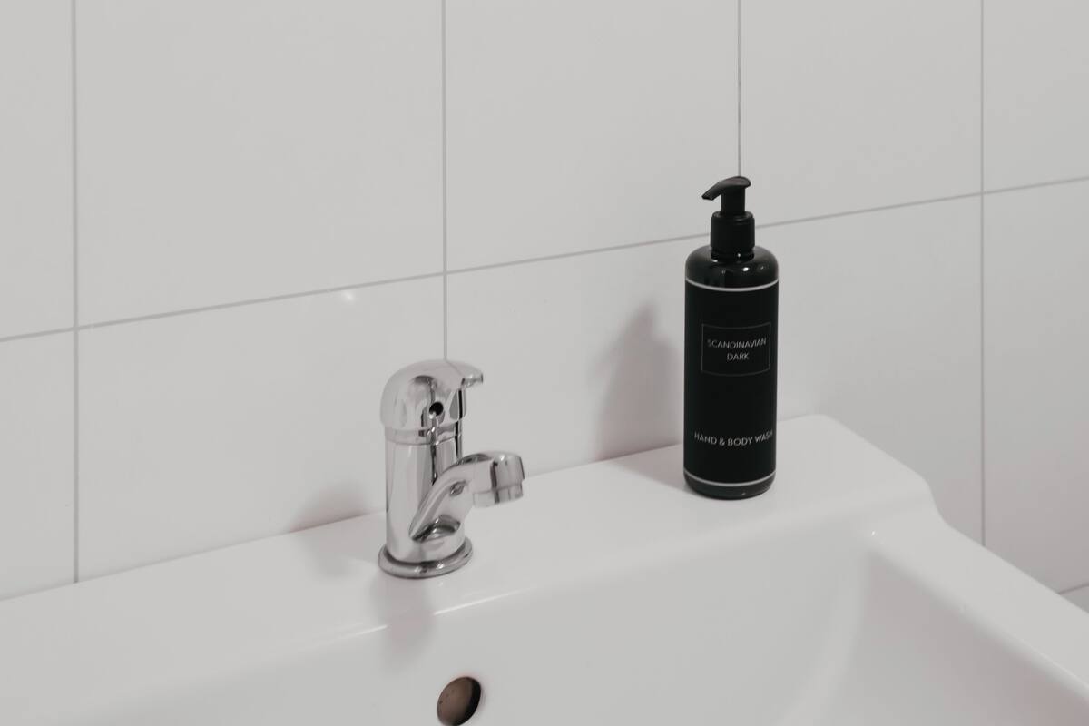 Un baño con un lavabo blanco, un grifo cromado y una botella negra de jabón de manos y cuerpo.