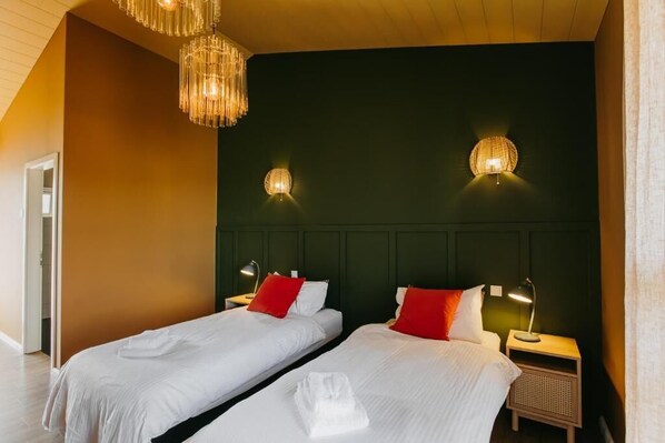 A hotel room with two beds, each with white linens and red pillows, a dark green headboard, and two wall-mounted lamps. - Guesthouse Hill (Hrunamannahreppur)