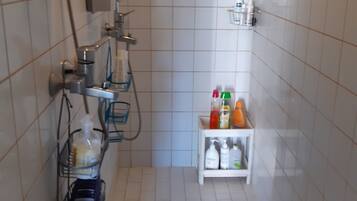 Un pequeño espacio de ducha con azulejos, un cabezal de ducha manual, un grifo empotrado en la pared y un estante con artículos de aseo.