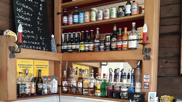 Een bar met flessenkasten vol diverse drankjes, een krijtbordmenu en een betaalautomaat.
