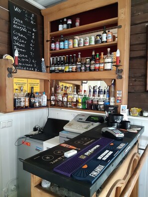 Een bar met flessenkasten vol diverse drankjes, een krijtbordmenu en een betaalautomaat.