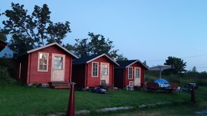 Drie kleine, rode hutten met genummerde deuren, een grindpad en een gazon.