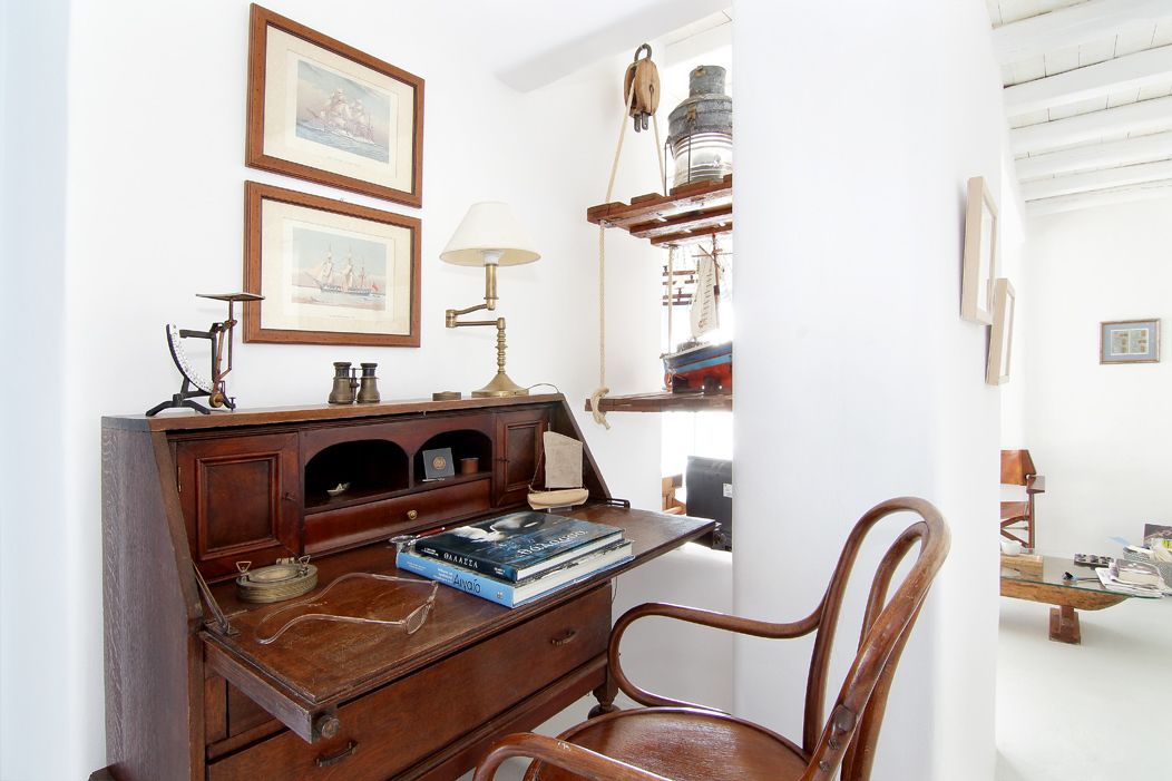 A study room with a wooden desk, a chair, a lamp, and framed pictures on the wall.