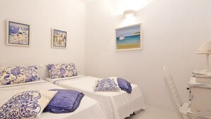 Una stanza con due letti, ognuno con una coperta a motivi bianchi e azzurri e cuscini coordinati. Tre quadri appesi alla parete raffigurano scene costiere.