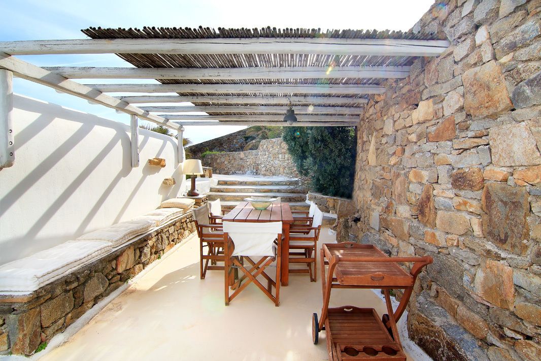 An outdoor patio with stone walls, wooden furniture, and a pergola.