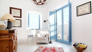 Un soggiorno luminoso con un divano bianco, un mobile in legno, un tappeto decorato e un'ampia finestra con persiane blu.