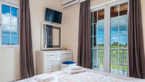A bedroom with a bed, a dresser, a mirror, and a balcony with a view. - Zante 5 bedroom Villa with private pool and basketball court (Zakynthos)