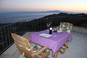 Une table dressée avec une nappe violette, deux chaises, une bouteille de vin et des verres, le tout sur un balcon donnant sur un paysage magnifique.