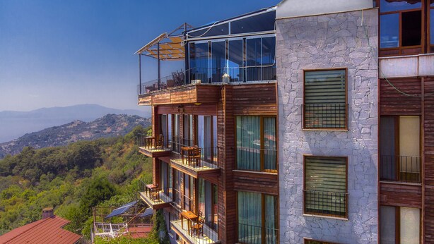 A multi-story building with balconies, large windows, and a view of a mountainous landscape. - Assos Kayalar Terrace Boutique Hotel (Ayvacik)