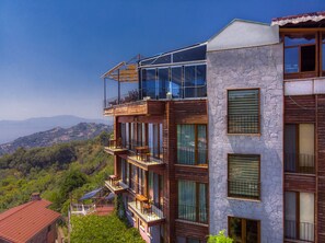 A multi-story building with balconies, large windows, and a view of a mountainous landscape. - Assos Kayalar Terrace Boutique Hotel (Ayvacik)