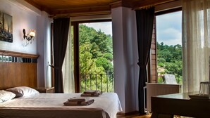A bedroom with a large bed, a wooden headboard, a nightstand, a table, and a view of a lush green landscape through a balcony. - Assos Kayalar Terrace Boutique Hotel (Ayvacik)