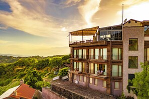 Un immeuble à plusieurs étages doté de balcons, de grandes fenêtres et offrant une vue sur un paysage vallonné.