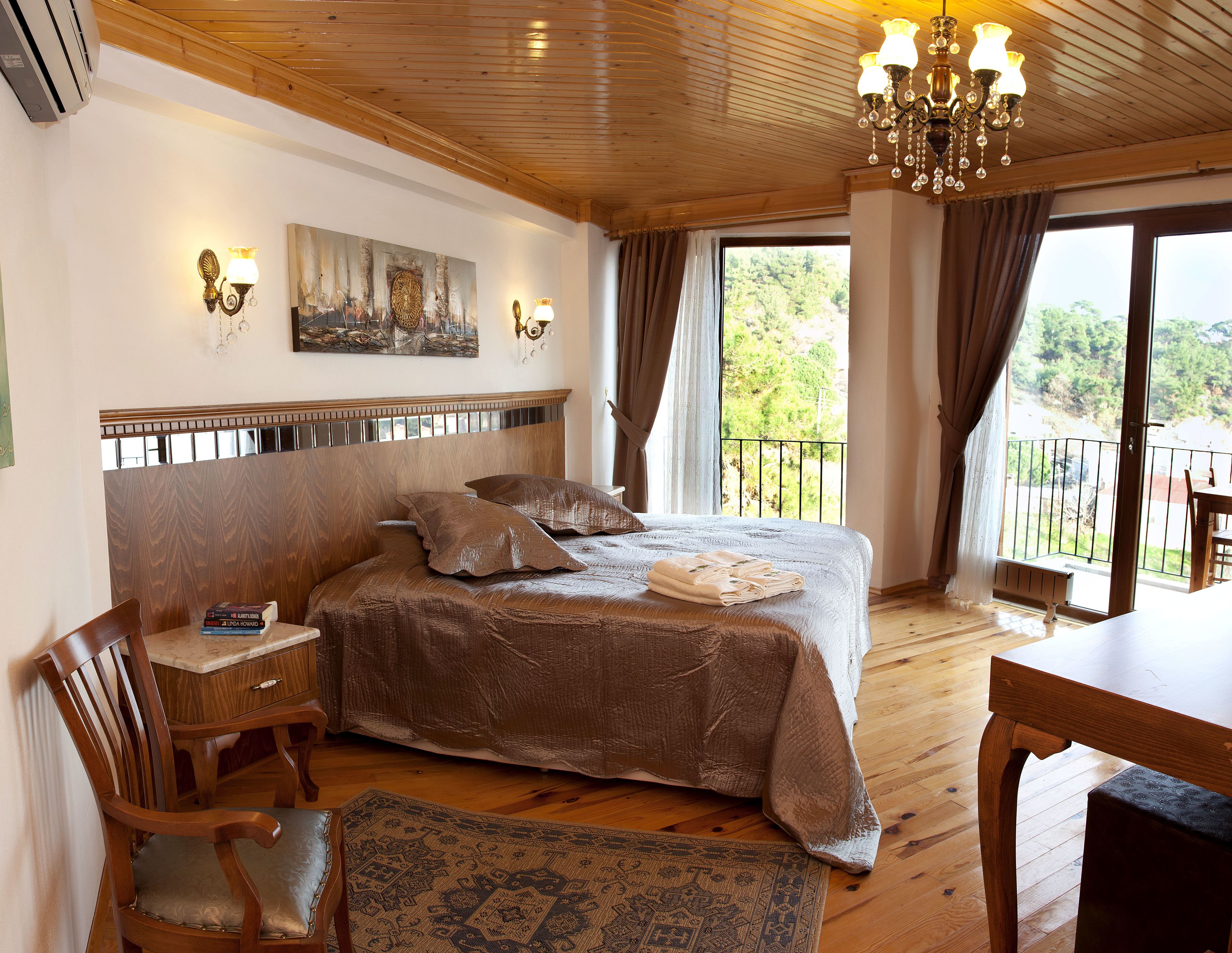 A bedroom with a large bed, a wooden headboard, a painting on the wall, and a balcony with a view of greenery.