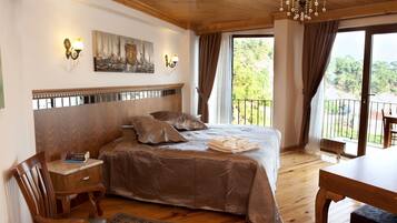 A bedroom with a large bed, a wooden headboard, a painting on the wall, and a balcony with a view of greenery.