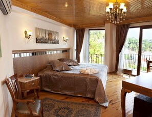 Un dormitorio con una cama grande, cabecera de madera, un cuadro en la pared y un balcón con vistas a la vegetación.