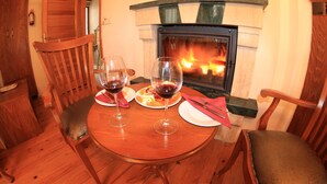 A wooden dining table with two wine glasses and plates, a fireplace, and wooden chairs. - Assos Kayalar Terrace Boutique Hotel (Ayvacik)