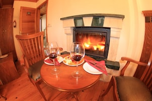 Una mesa de comedor de madera con dos copas de vino y platos, una chimenea y sillas de madera.