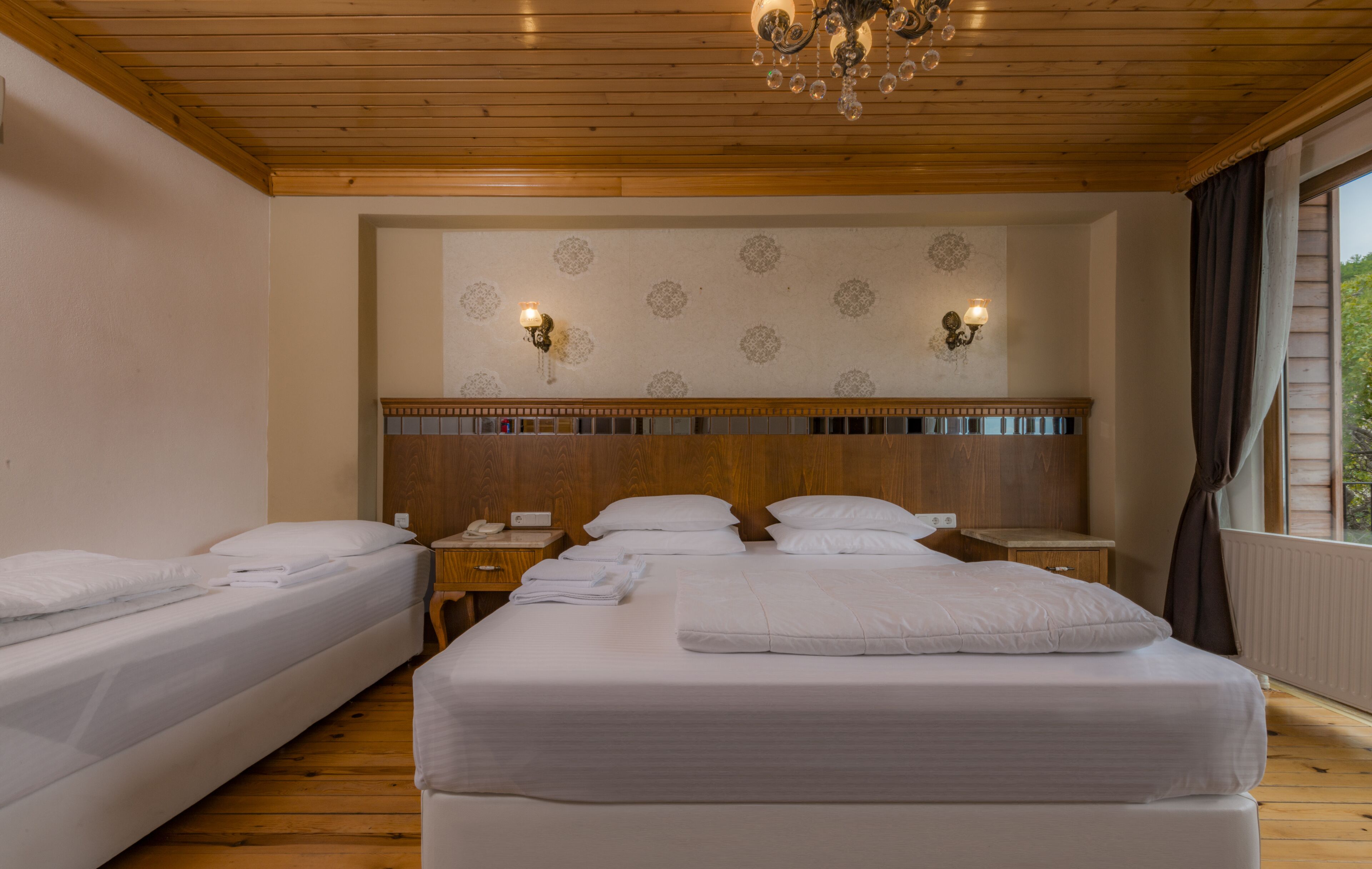 Habitación de hotel con dos camas, suelo de madera, un candelabro y un papel tapiz estampado.