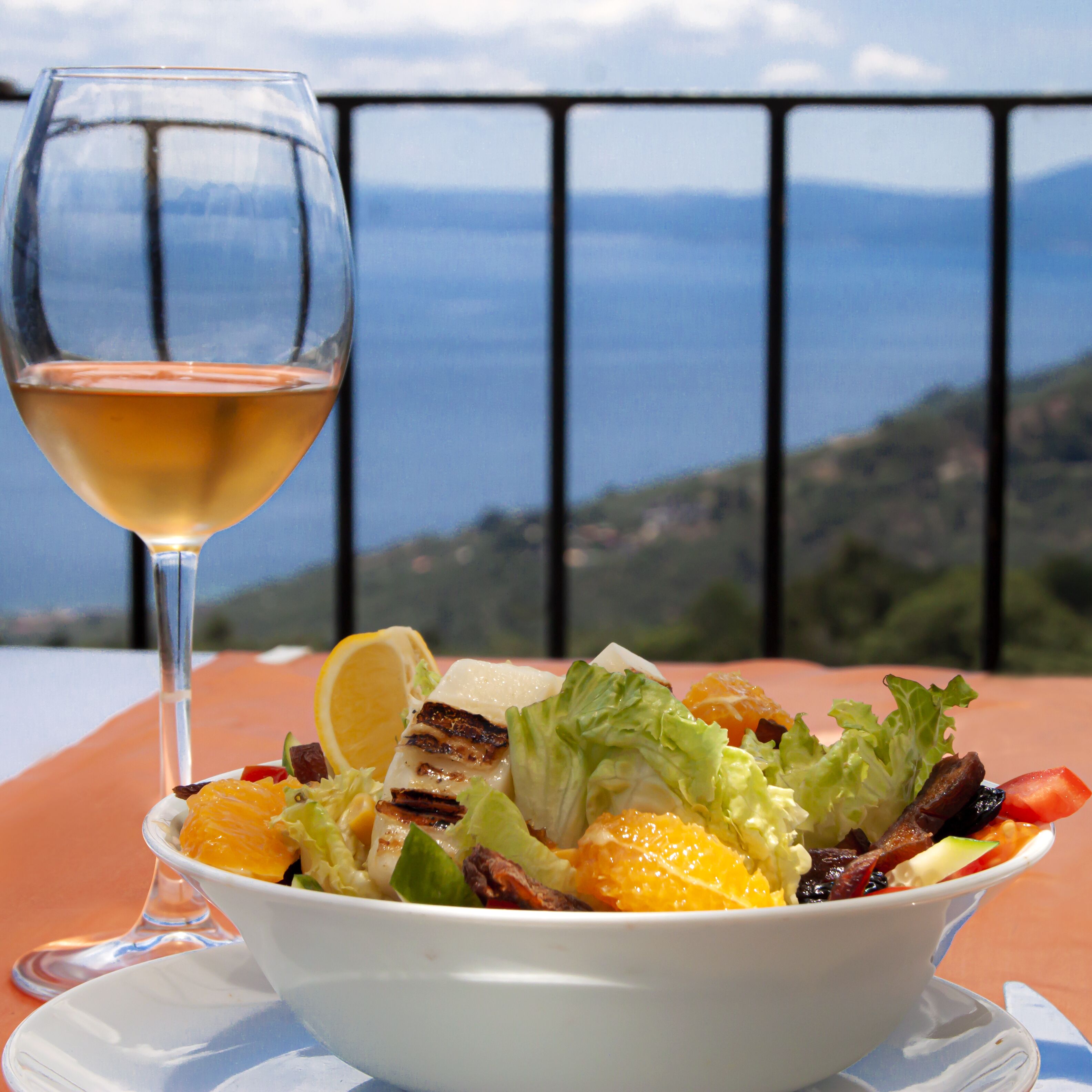 Ensalada con carne a la parrilla, verduras y una copa de vino sobre una mesa con vistas panorámicas.