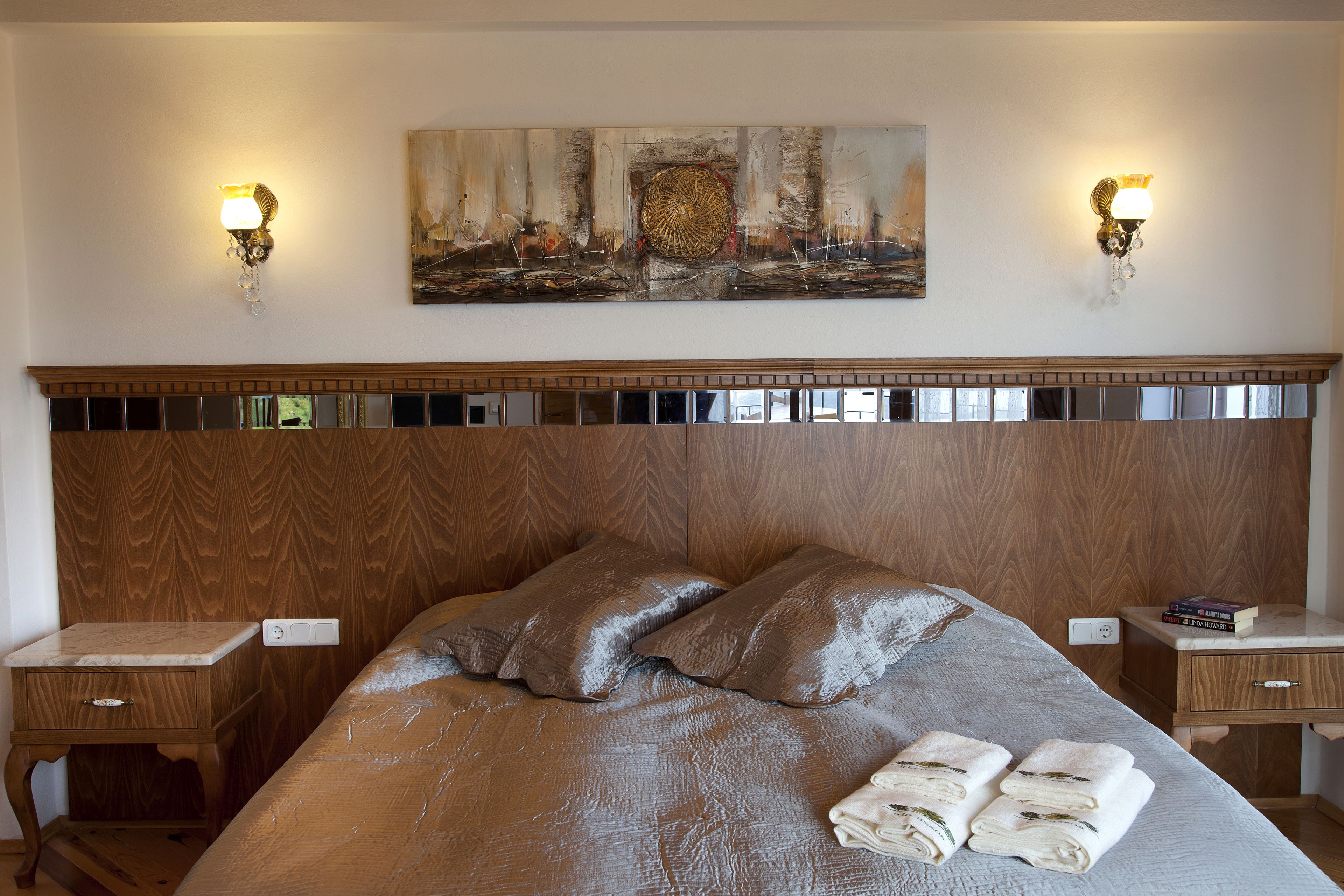 Un lit bien fait, avec une tête de lit, deux tables de chevet et un tableau accroché au mur au-dessus.