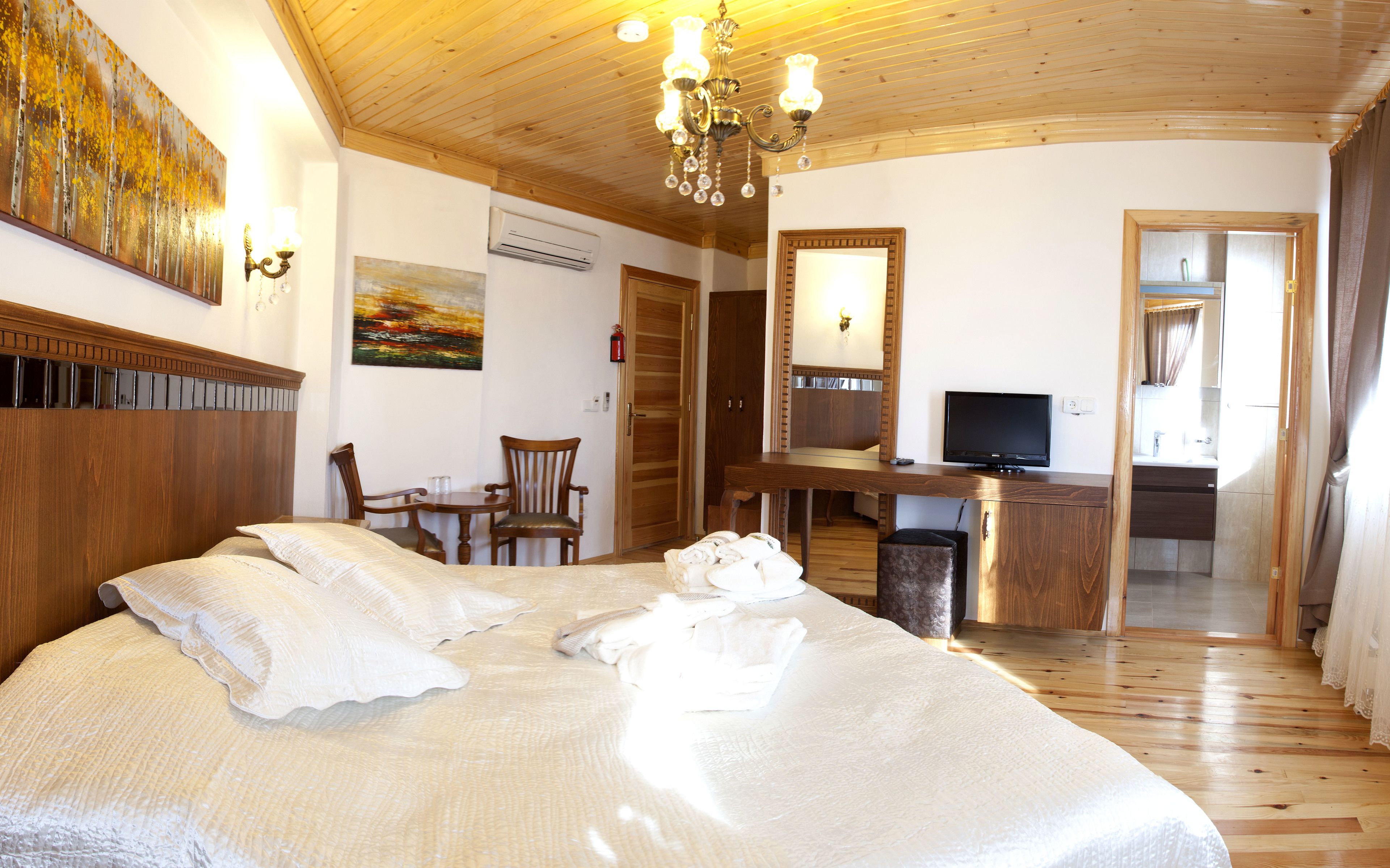 A hotel room with a large bed, a desk with a TV, a chair, a small table, and a painting on the wall.